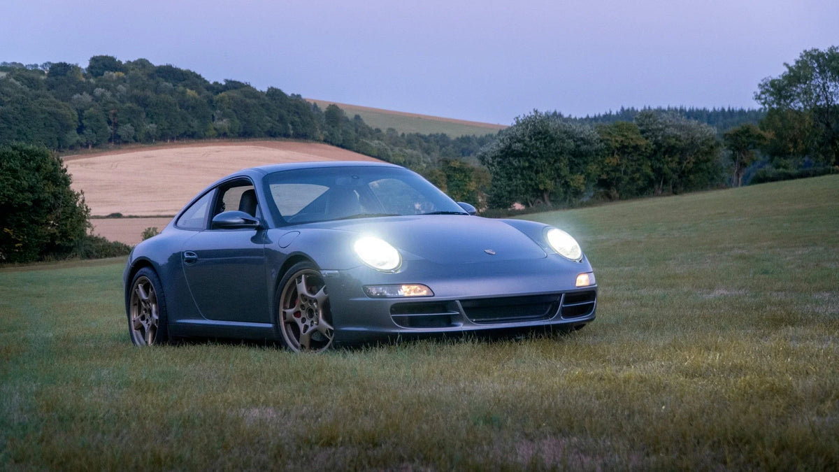 A blue Porsche parked on grass at dusk